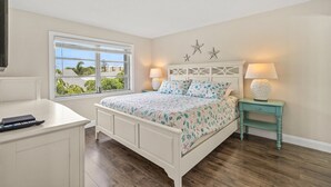 A bedroom with a bed, a nightstand, a desk, and a window with a view. - Pristine Tropical Condo w/ Heated Pool. Walk to Beach, Dining, Shopping & More! VH 304C (Siesta Key)
