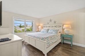 A bedroom with a bed, a nightstand, a desk, and a window with a view.