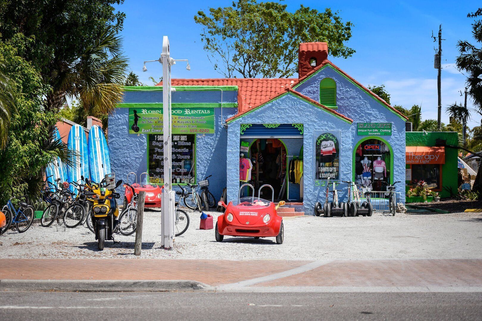 Een kleurrijk gebouw met een rood dak, een bord met 'Robin Food Rentals' dat jetski's, paddleboards en scooters aanbiedt, en een winkel die T-shirts en souvenirs verkoopt.