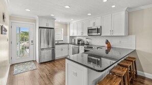 A modern kitchen with white cabinets, stainless steel appliances, and a granite countertop. - Pristine Tropical Condo w/ Heated Pool. Walk to Beach, Dining, Shopping & More! VH 304C (Siesta Key)