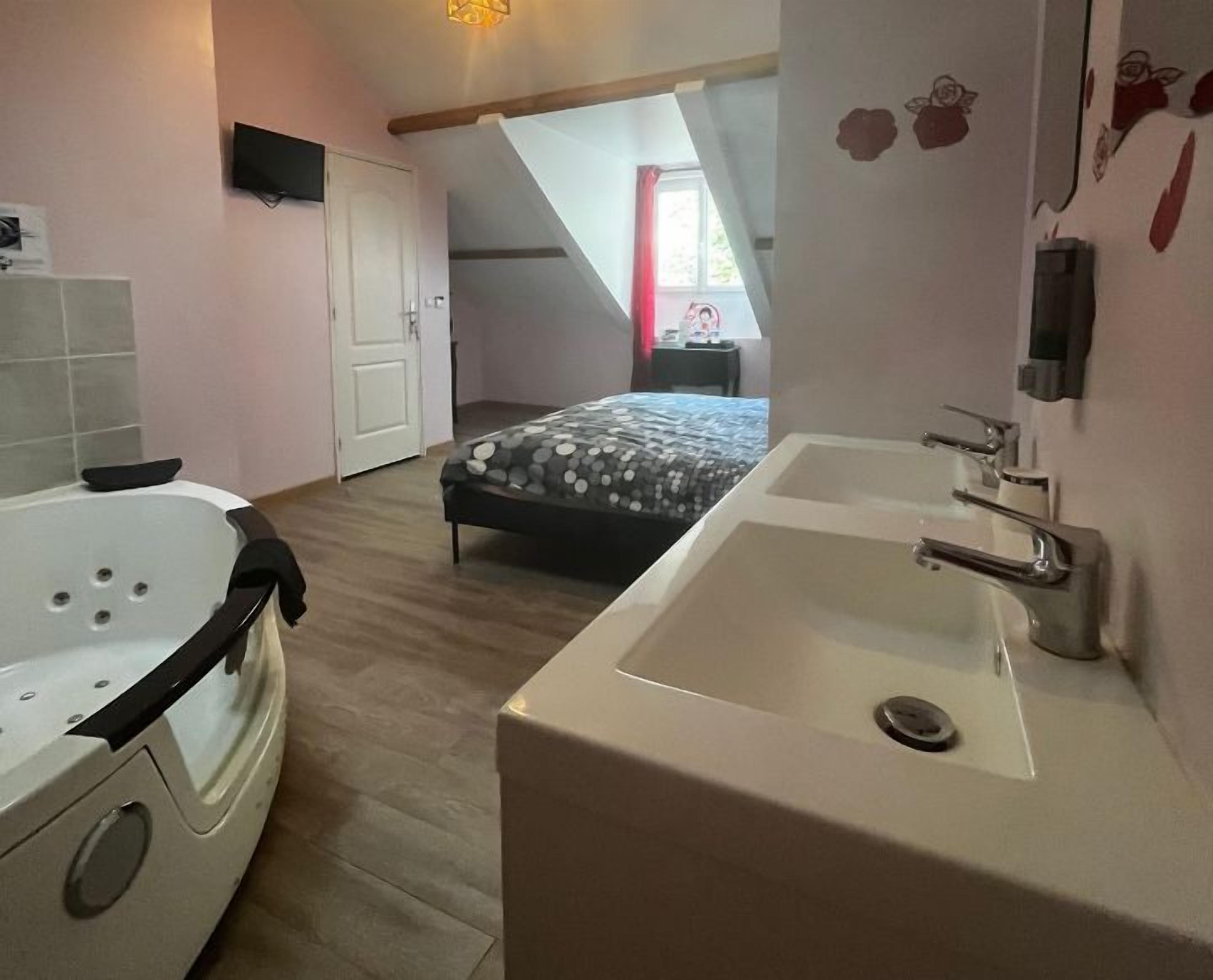 A bedroom with a large window, a bed, a bathtub, and a sink.