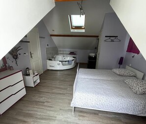 A bedroom with a bed, a small bathroom, and a hot tub. The room has a sloped ceiling with a skylight. - Le petit manoir (Farceaux)