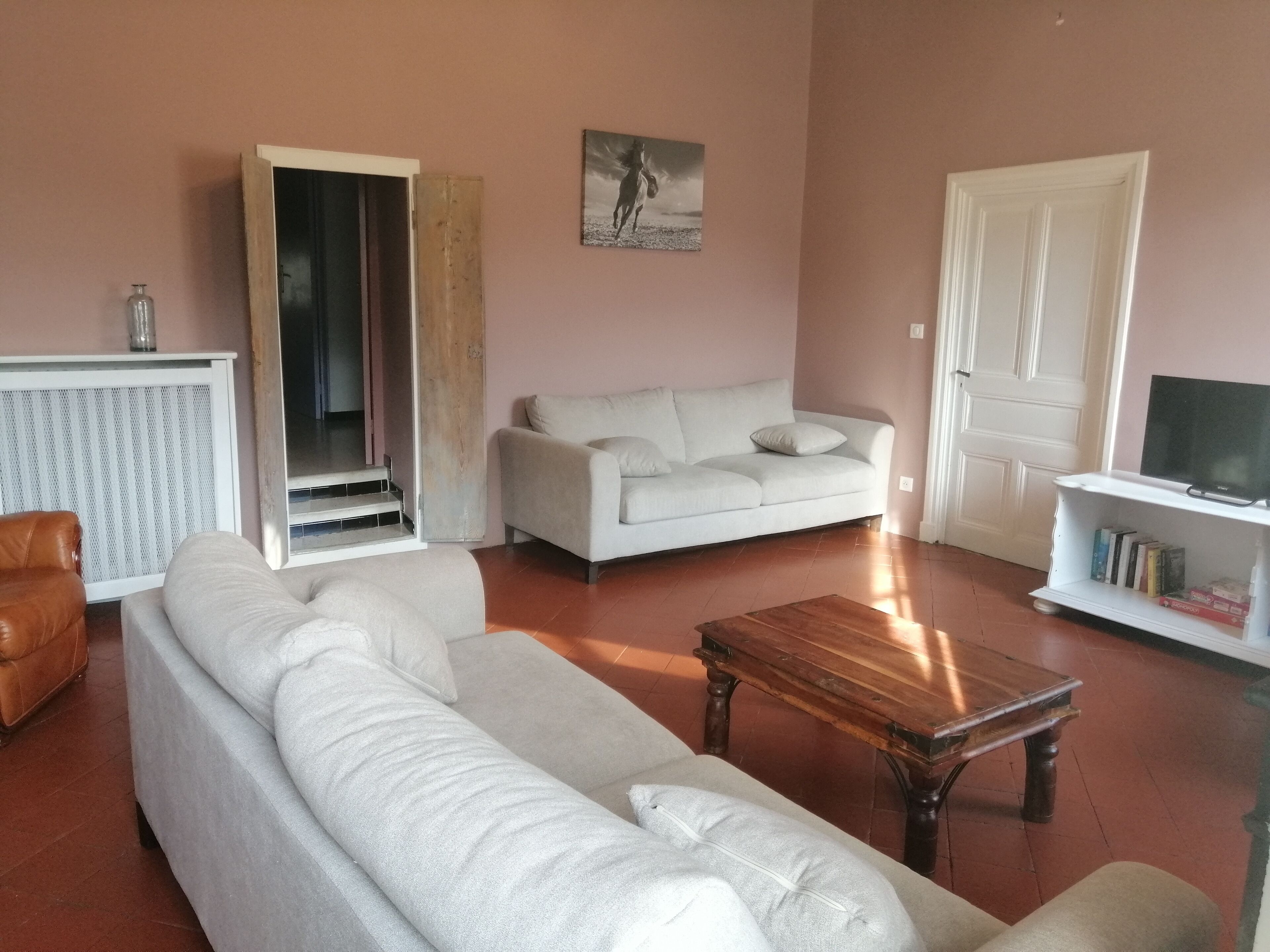 Ein Wohnzimmer mit einer Couch, einem Couchtisch, einer TV-Bank mit Büchern und einer Tür.