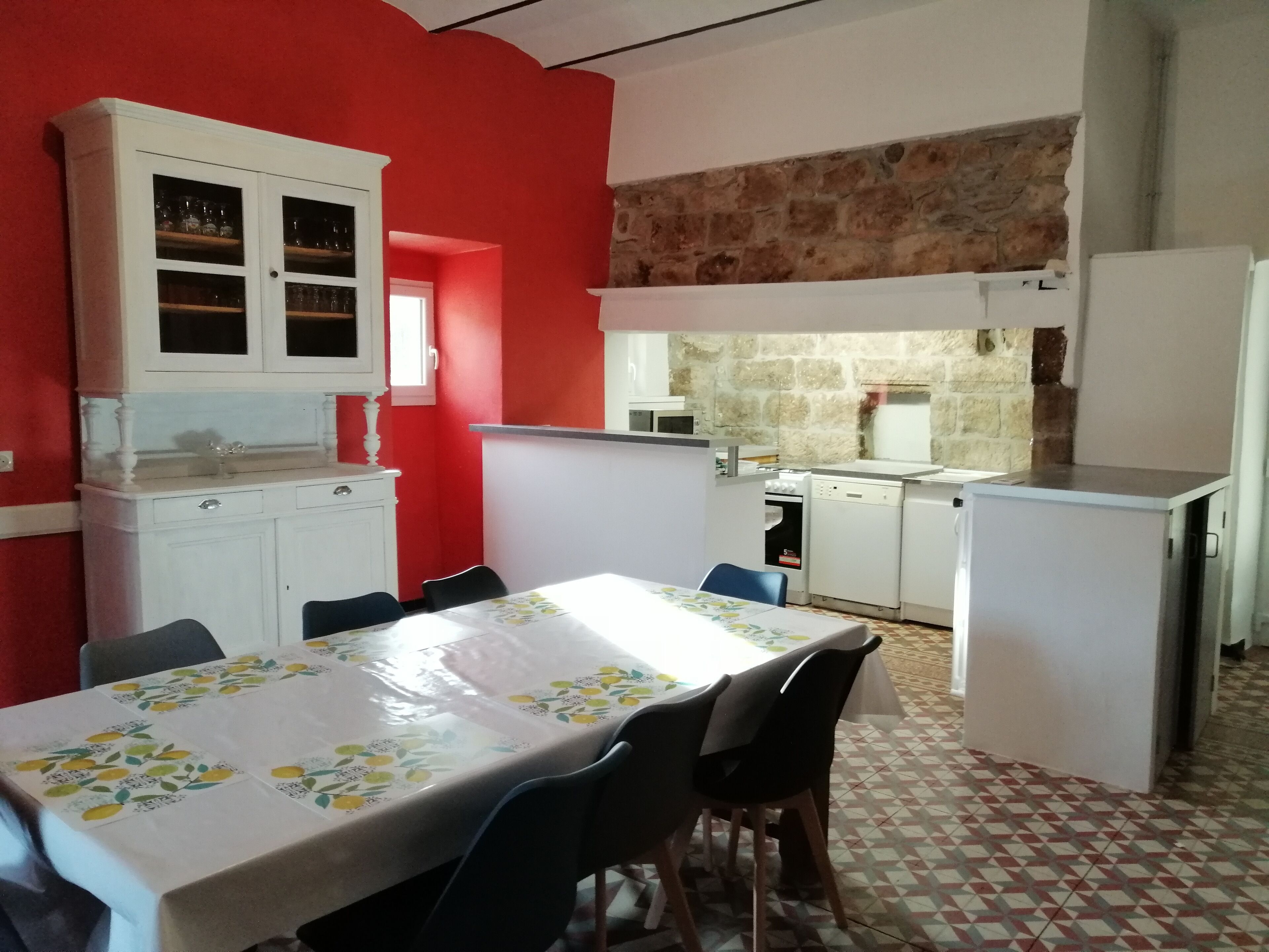 Een compacte keuken met witte kasten, een eettafel met stoelen en een rode accentmuur.