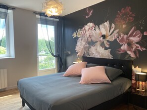 Un dormitorio con una cama grande, una ventana con cortinas, un mural floral en la pared y una lámpara de noche.