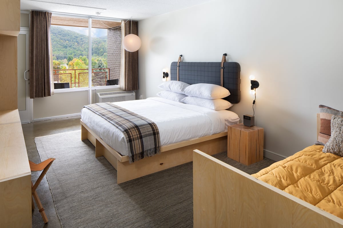 Quarto de hotel moderno com uma cama grande, uma escrivaninha e vista para o exterior.