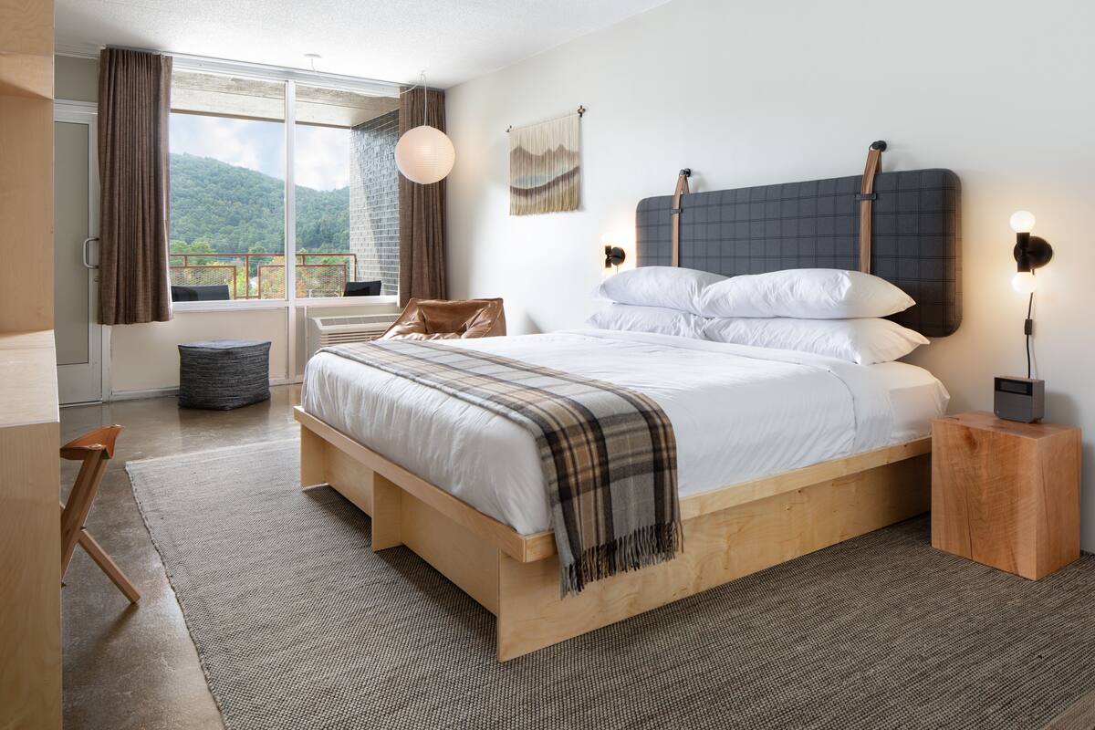 Quarto moderno com uma cama grande, cabeceira de madeira, mesas de cabeceira e vista para o exterior.