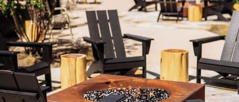 An outdoor seating area with black chairs, a central fire pit, and wooden stools.