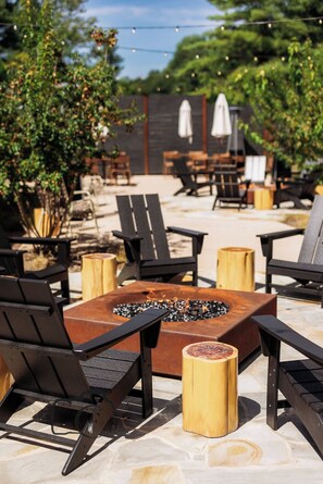 An outdoor seating area with black chairs, a central fire pit, and wooden stools.