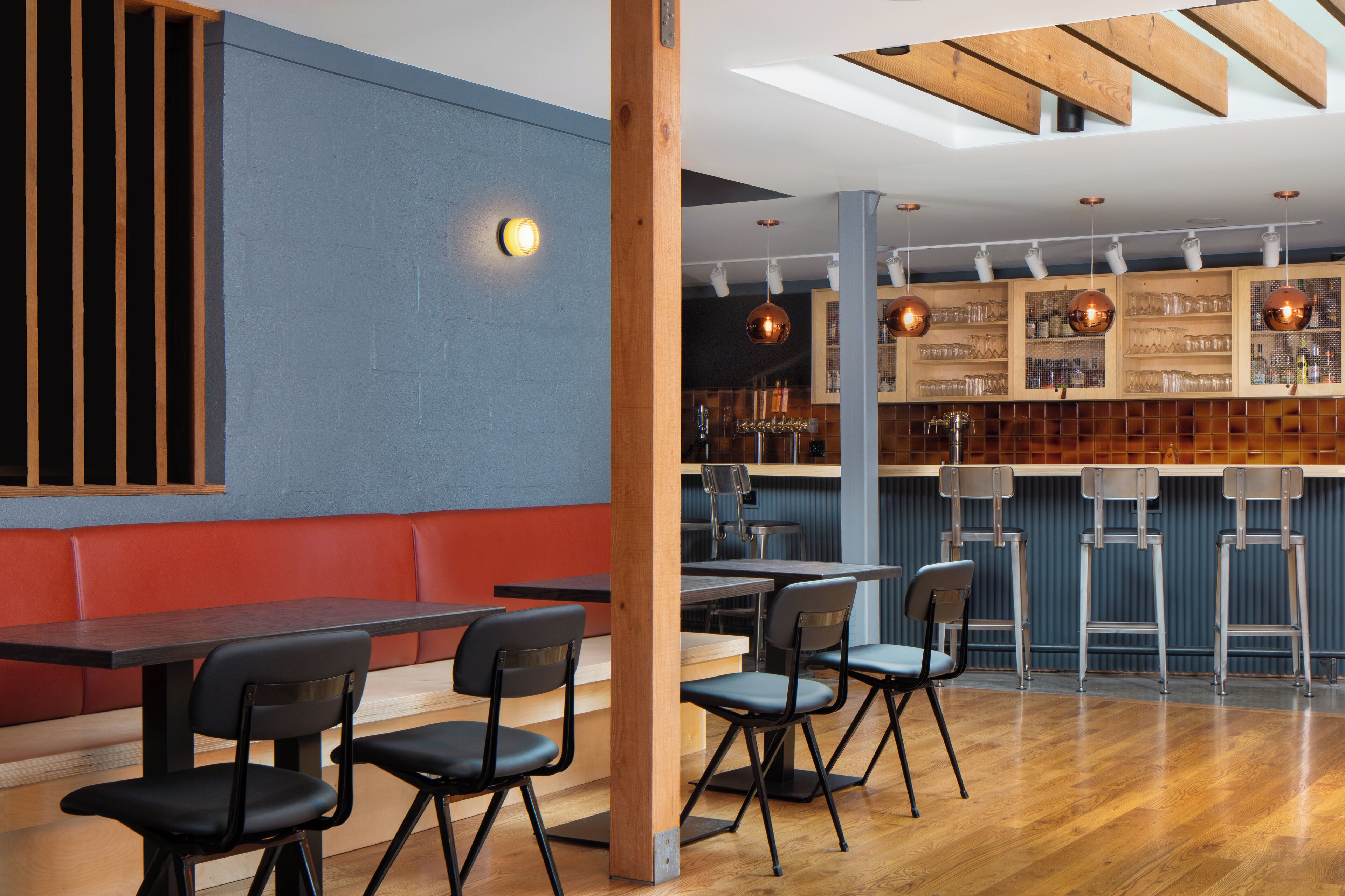 A modern bar area with wooden beams, a blue wall, and a bar counter with stools.
