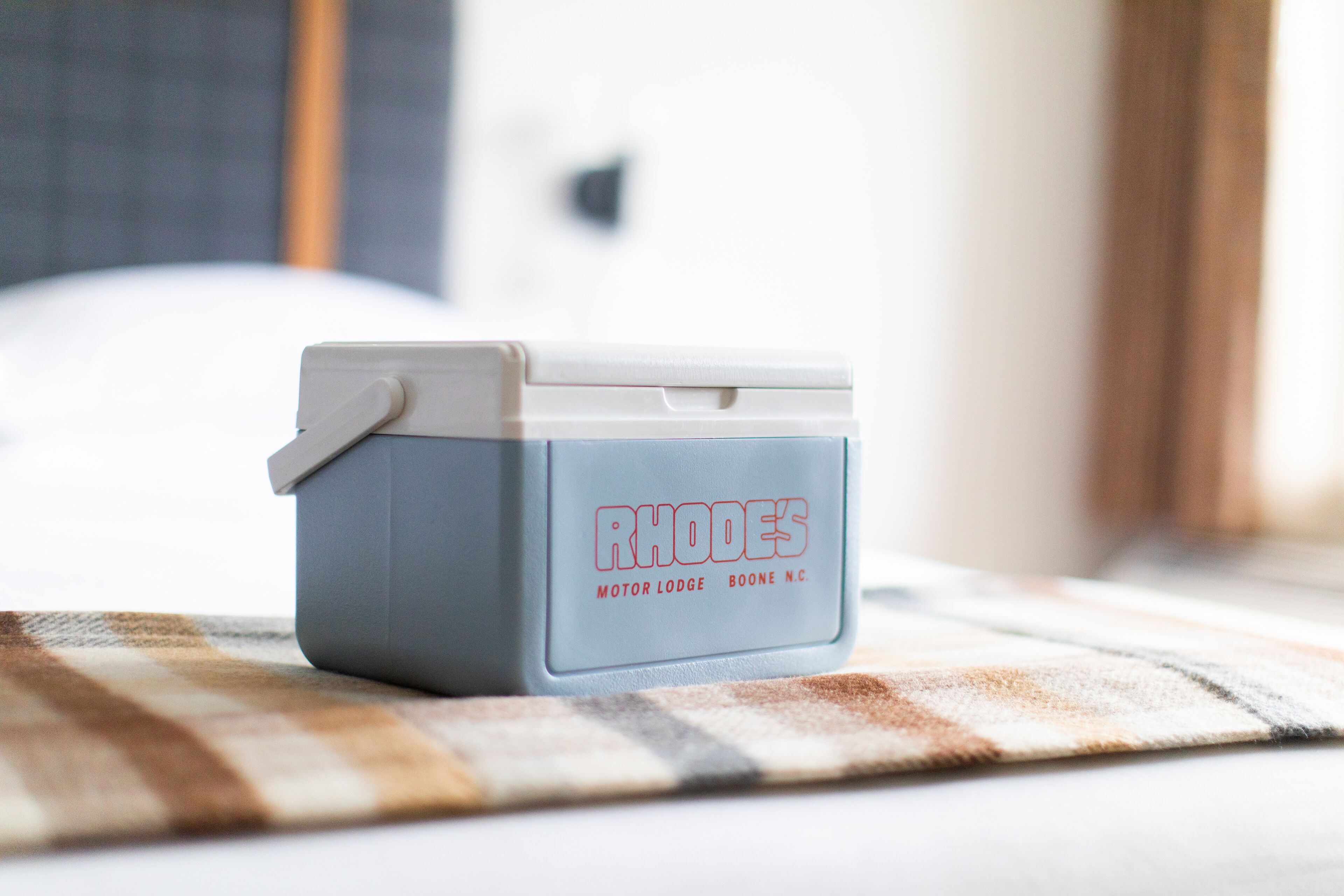 Une petite glacière bleu clair, sur laquelle on peut lire « RHODES MOTOR LODGE BOONE NC », est posée sur une nappe à carreaux.
