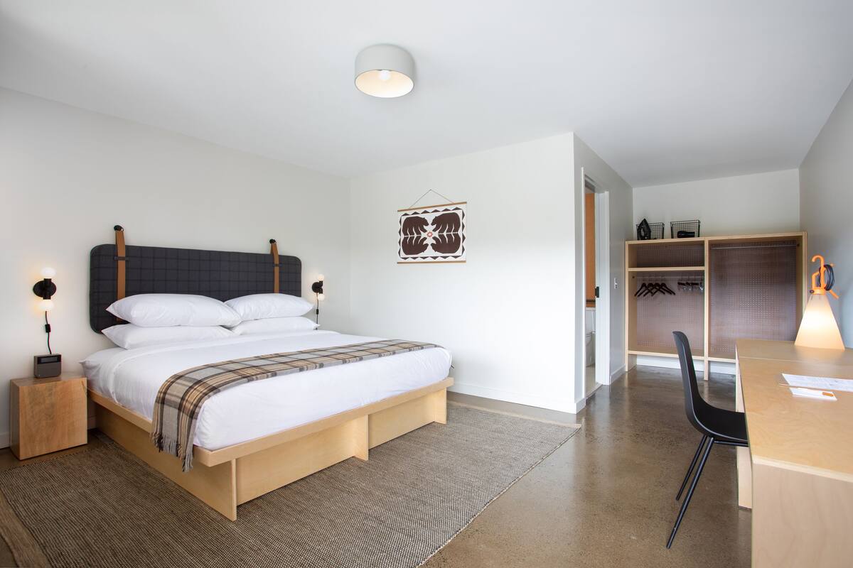 Quarto moderno com cama, mesas de cabeceira, escrivaninha e cadeira.