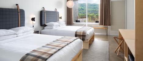 A hotel room with two beds, a desk, a chair, a large window with curtains, and a view of greenery.