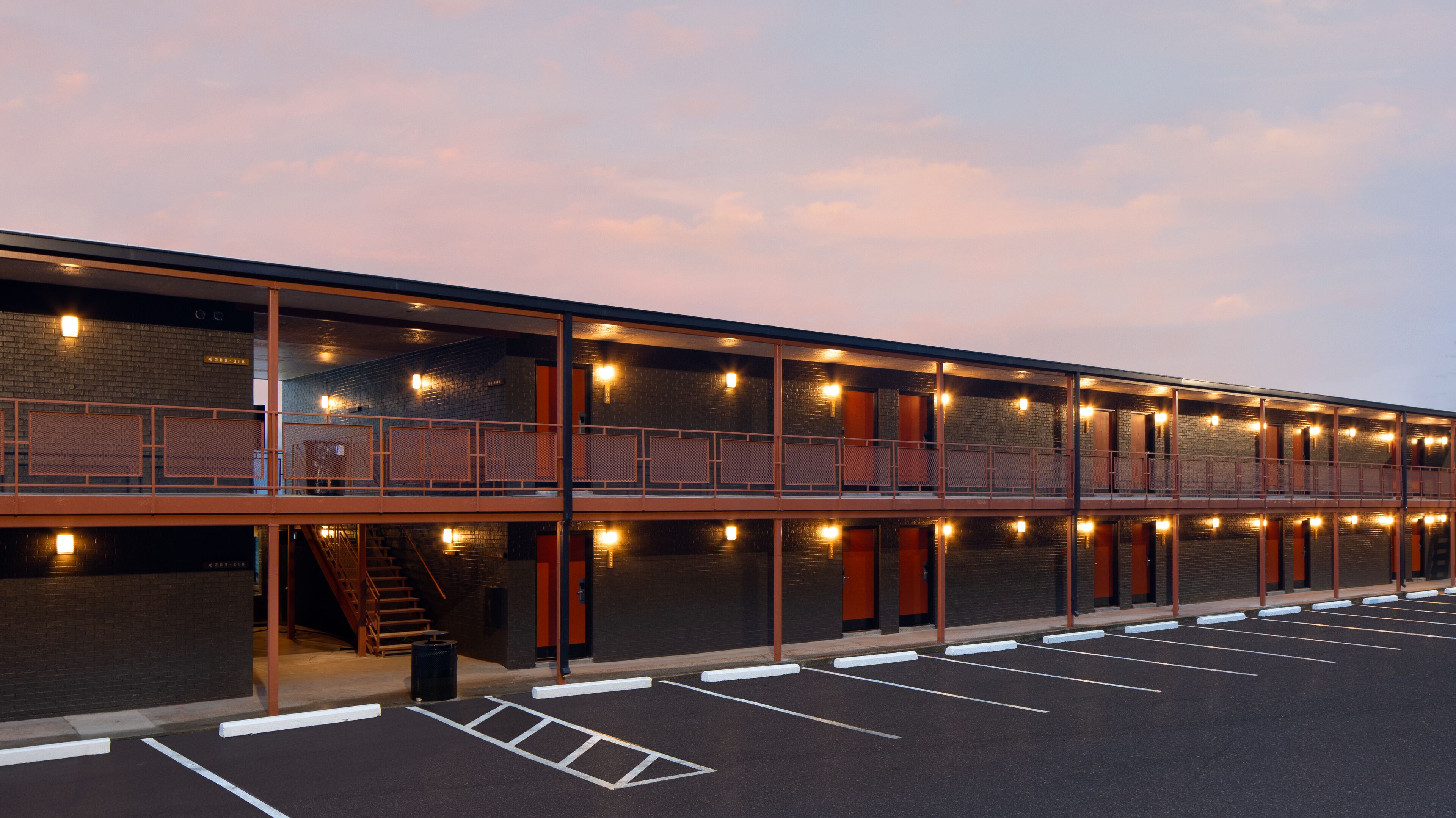 Un motel à plusieurs étages, doté d’un balcon au rez-de-chaussée et d’un parking à l’avant.