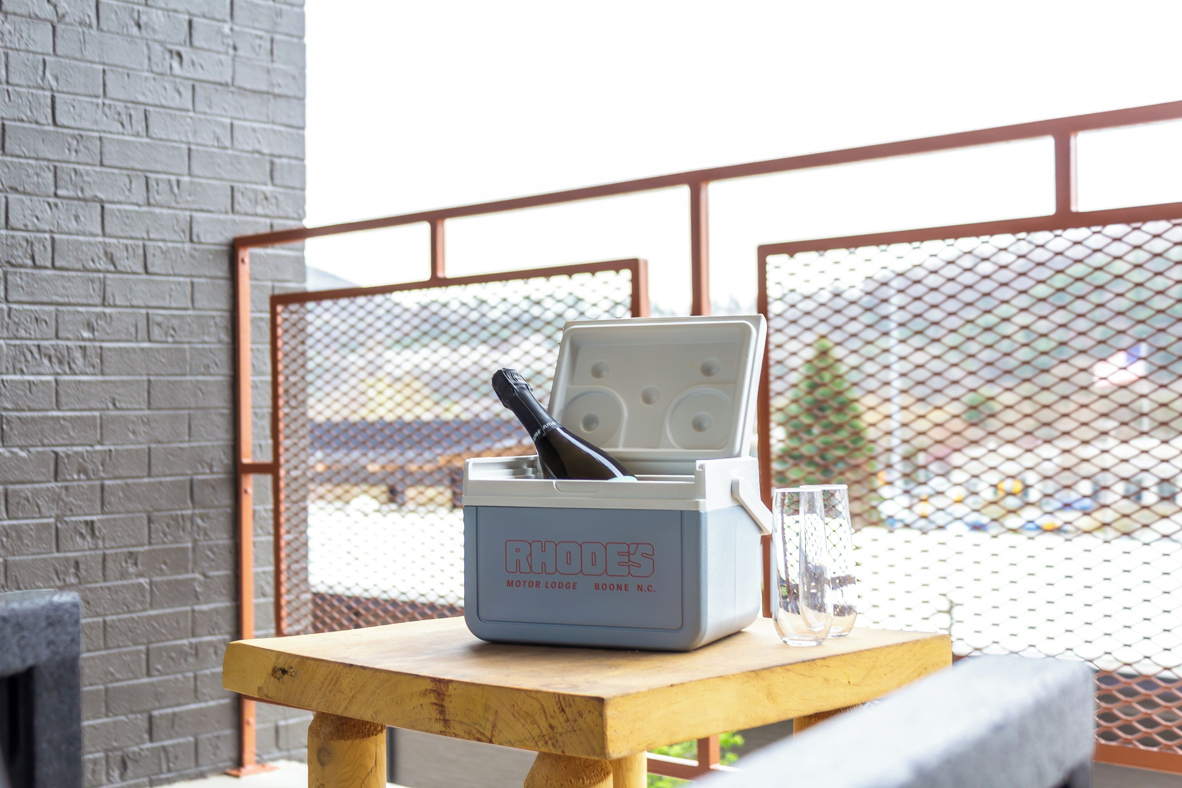 Une glacière portative sur laquelle est inscrit le texte « RHODE'S MOTOR LODGE BOONE N.C. », posée sur une table en bois.
