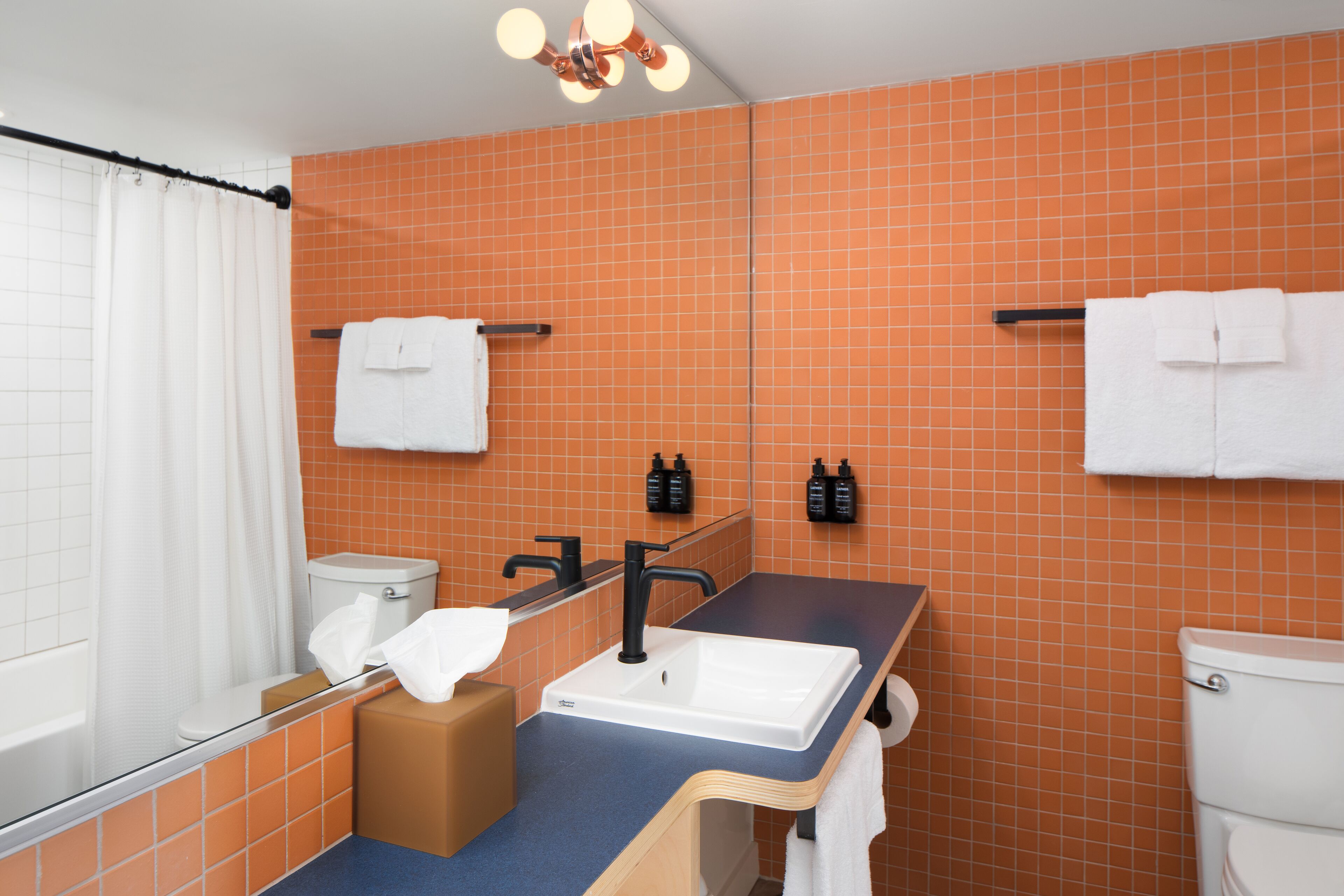 A bathroom with orange tiled walls, a white sink, a black faucet, and a bathtub.