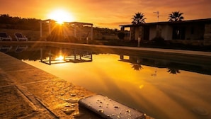 Un capvespre sobre una piscina amb gandules i un edifici al fons.