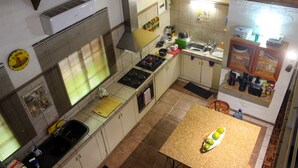 Une cuisine équipée d’une cuisinière, d’un évier et de divers appareils électroménagers. On y trouve une fenêtre avec des stores, un plan de travail avec une planche à découper et une table sur laquelle se trouve un saladier rempli de fruits.