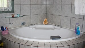 Une salle de bain avec une grande baignoire, une étagère en verre où sont rangés les articles de toilette, et une serviette accrochée au mur.
