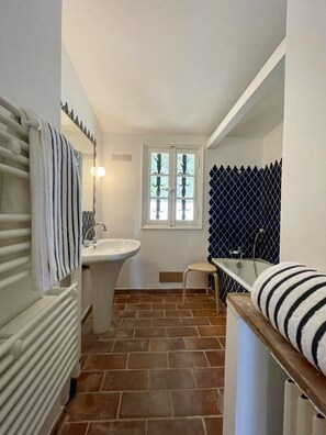 Bathroom features a white sink, mirror, and radiator, with a small stool and brown tile flooring.