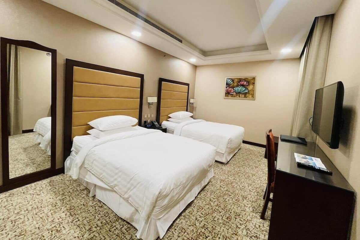 A hotel room with two beds, a television, a desk, and a mirror.