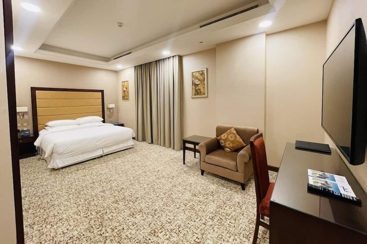 A hotel room with a bed, a desk, a chair, a television, and a carpeted floor.