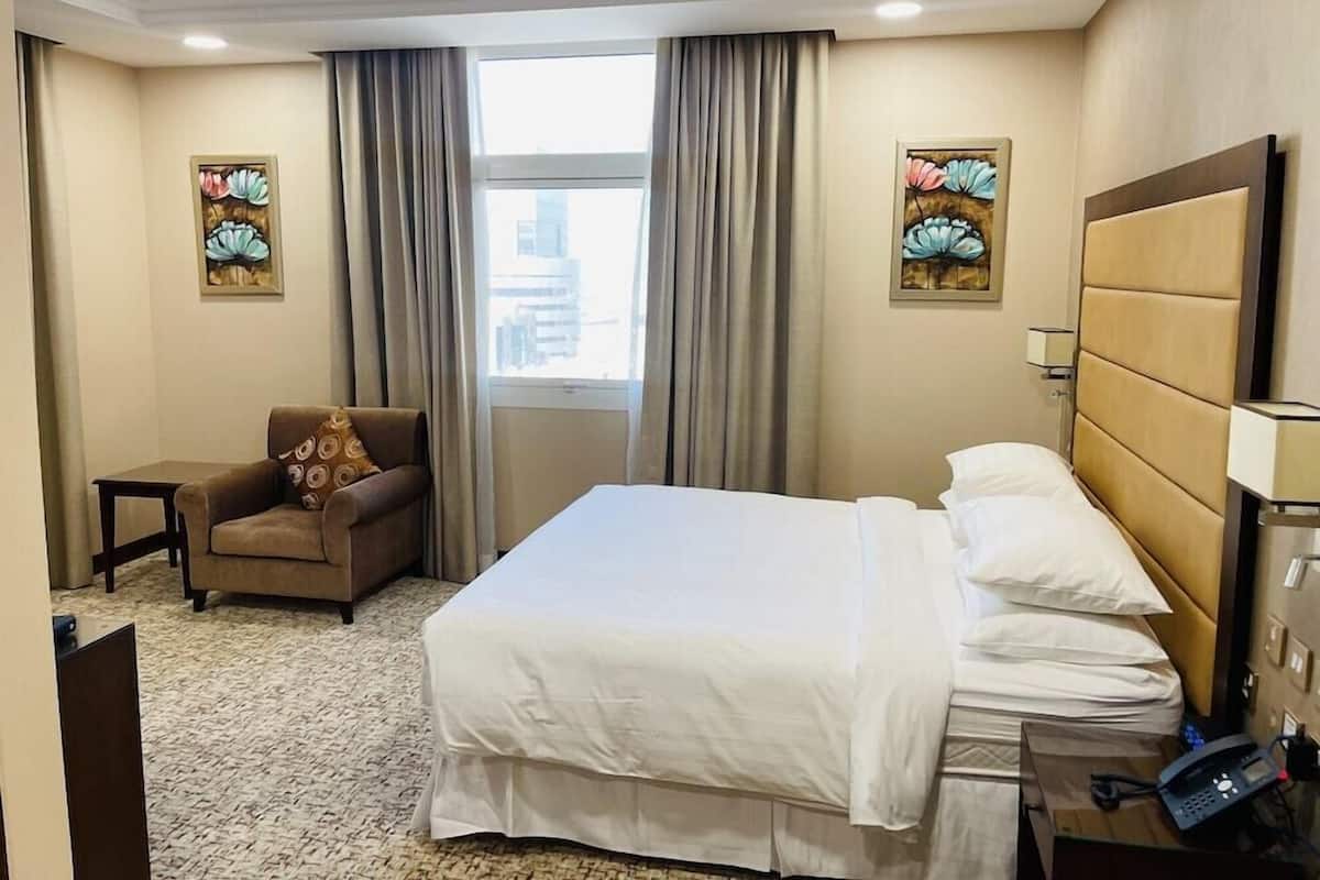 A hotel room with a bed, a chair, a desk, a telephone, and two paintings on the walls.