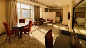 Habitación de hotel con zona de comedor, sofá, cama y un amplio ventanal.