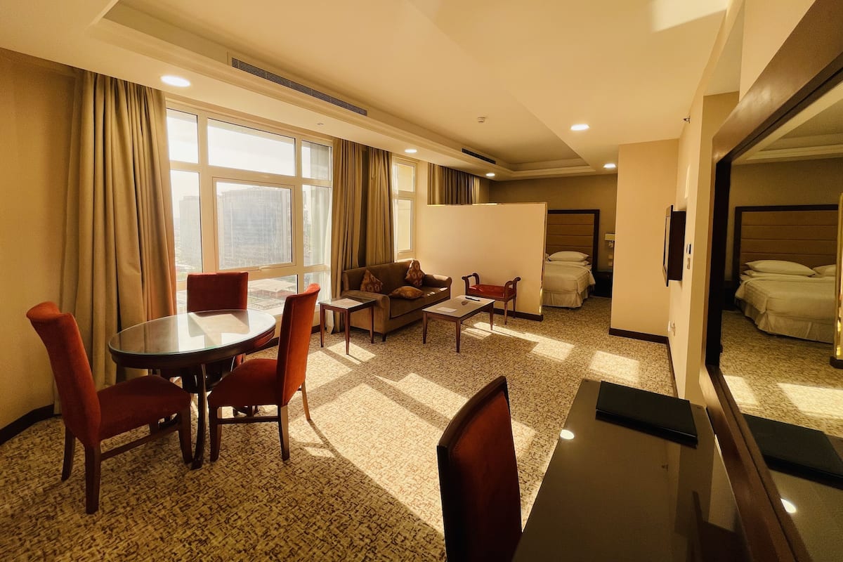 A hotel room with a dining area, a sofa, a bed, and a large window.