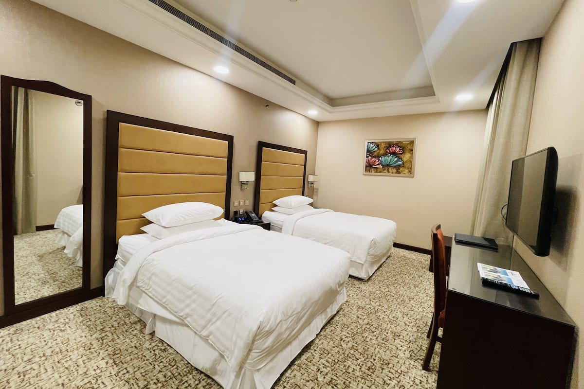 A hotel room with two beds, a large mirror, a flat-screen TV, and a small desk.