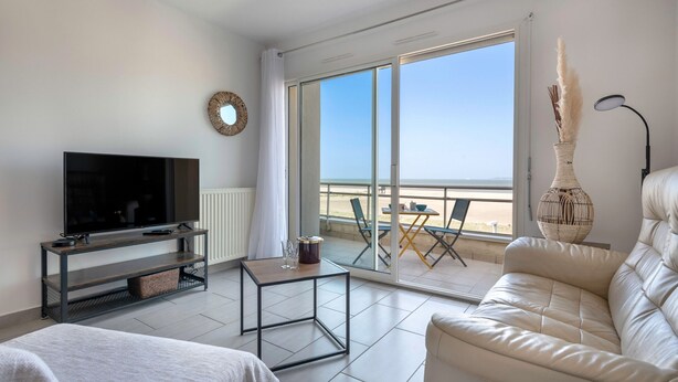 A modern living room with a flat-screen TV, a sofa, a coffee table, and a balcony with a view. - Facing the sea -  apartment for 2 (Saint-Brevin-les-Pins)