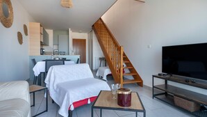 A modern living room with a sofa, a coffee table, a TV, and a staircase. - Facing the sea -  apartment for 2 (Saint-Brevin-les-Pins)