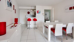 Cocina moderna con armarios blancos, taburetes rojos y un comedor con sillas blancas y cojines rojos.