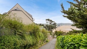 Un sendero estrecho bordeado por abundante vegetación y un edificio con techo triangular.