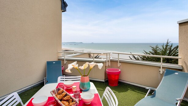 Un balcón con mesa lista para comer, una silla y vista al mar.