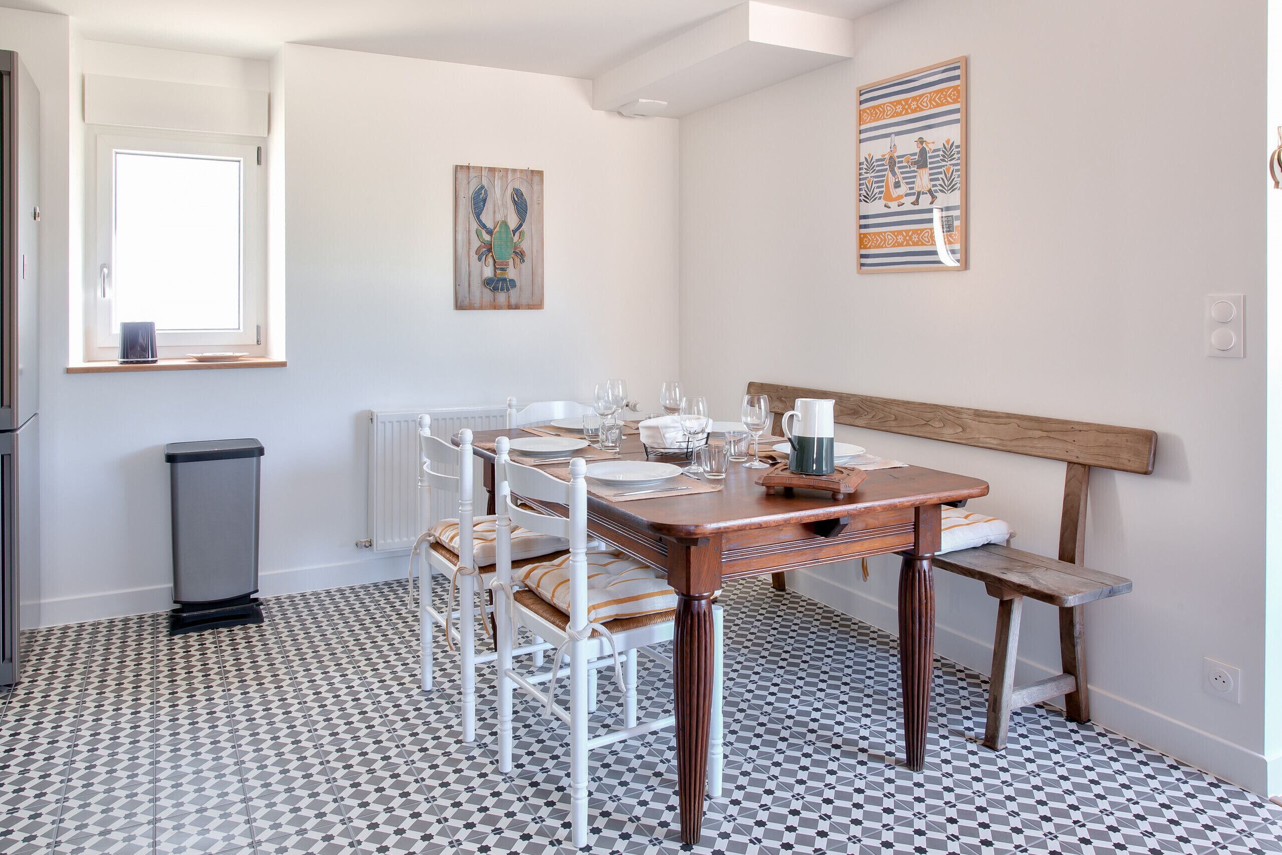 A dining area with a checkered floor, white chairs, a wooden table, and a bench.
