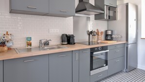 Eine moderne Küche mit grauen Schränken, einem Edelstahlkühlschrank, einem eingebauten Backofen und einer Kaffeemaschine.
