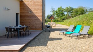 Un patio in legno con tavolo e sedie, un barbecue e due poltrone da relax.