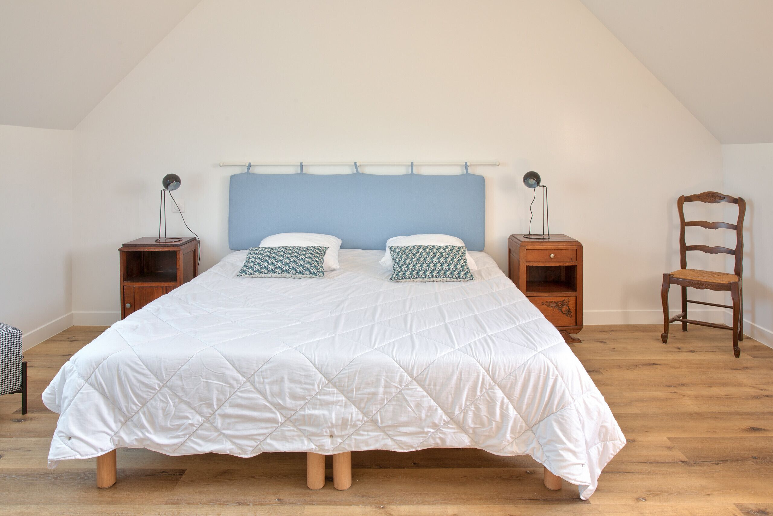 A bedroom with a bed, two bedside tables, a chair, and a wooden floor.