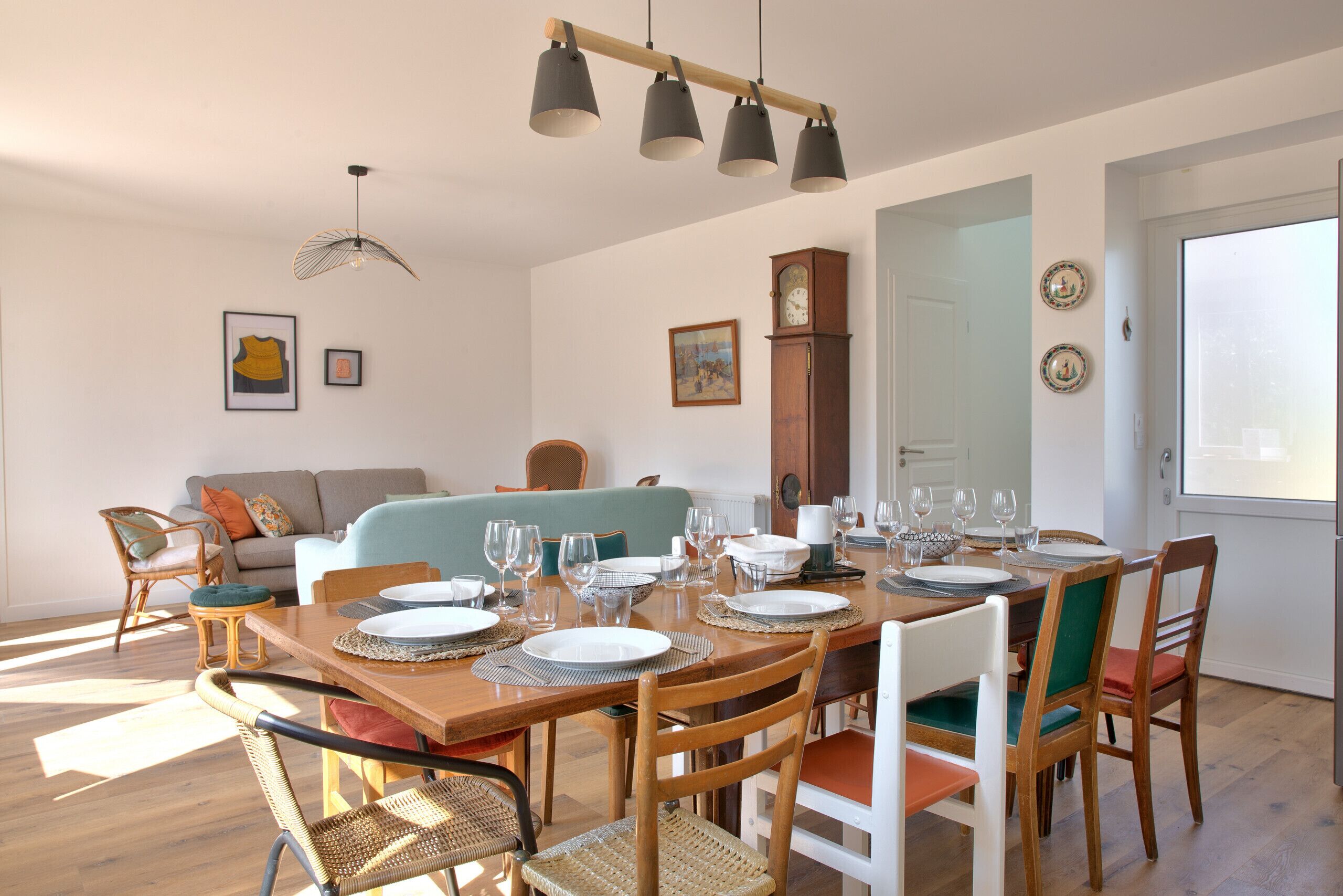 A dining area with a wooden table set for six, surrounded by wicker chairs and a wooden bench.