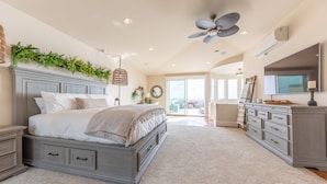 A bedroom with a large bed, a ceiling fan, a dresser, and a view of the outdoors. - Stunning Oceanfront Home w/ Panoramic Views (Oceanside)