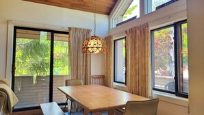 A dining area with a wooden table and benches, large windows with curtains, and a hanging light fixture. - Open concept, deck, fireplace, AC, pet-friendly, near Loon. C6301 by LRS (Lincoln)