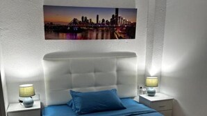 A neatly arranged bedroom with a cityscape view, a tufted headboard, and bedside lamps. - Rambla Apartment by the Sea (Alicante (Alacant))