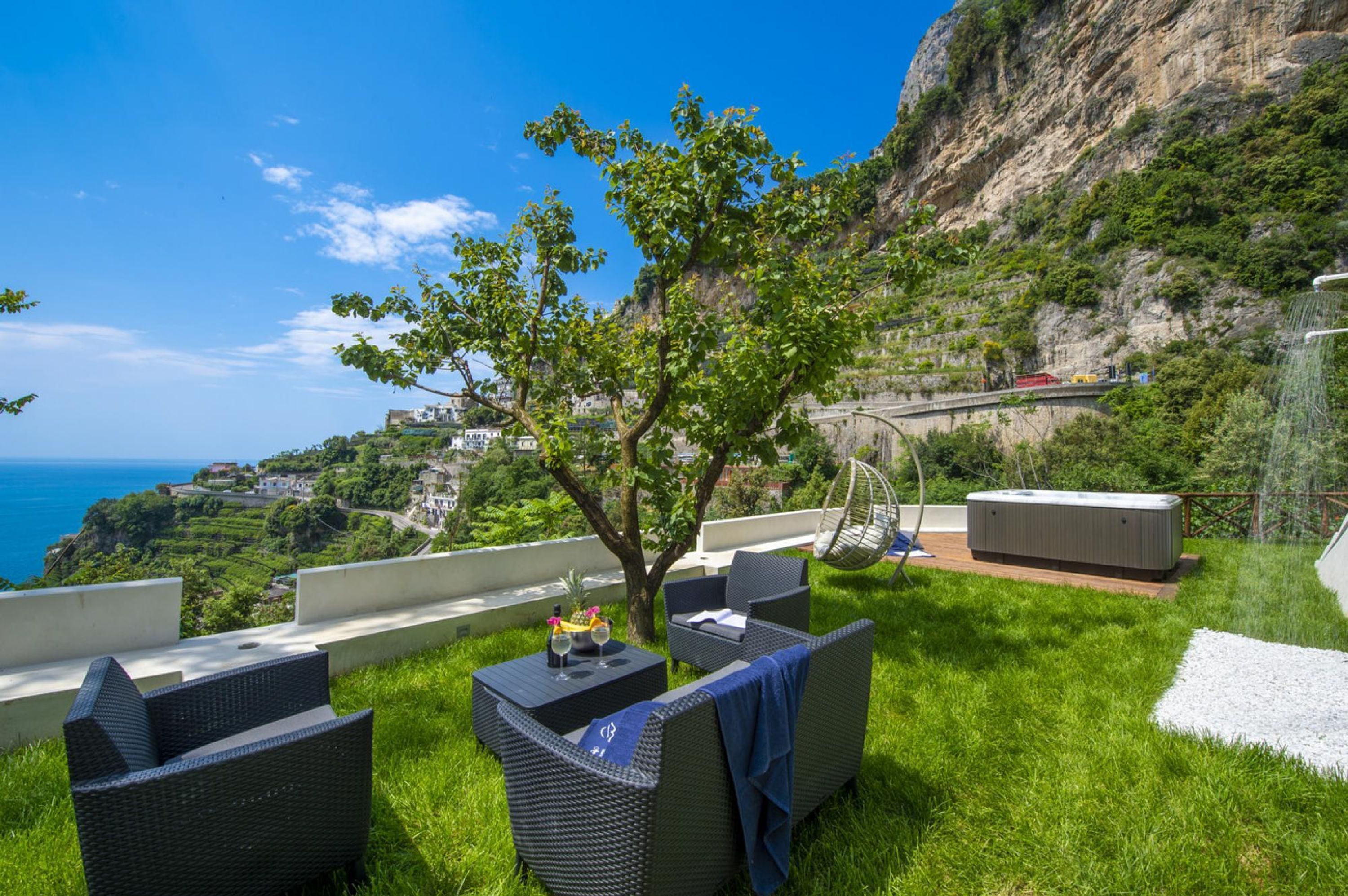 Una terraza con mobiliario de mimbre, una bañera de hidromasaje y vistas panorámicas de la costa.