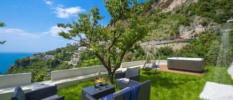 Una terraza con mobiliario de mimbre, una bañera de hidromasaje y vistas panorámicas de la costa.