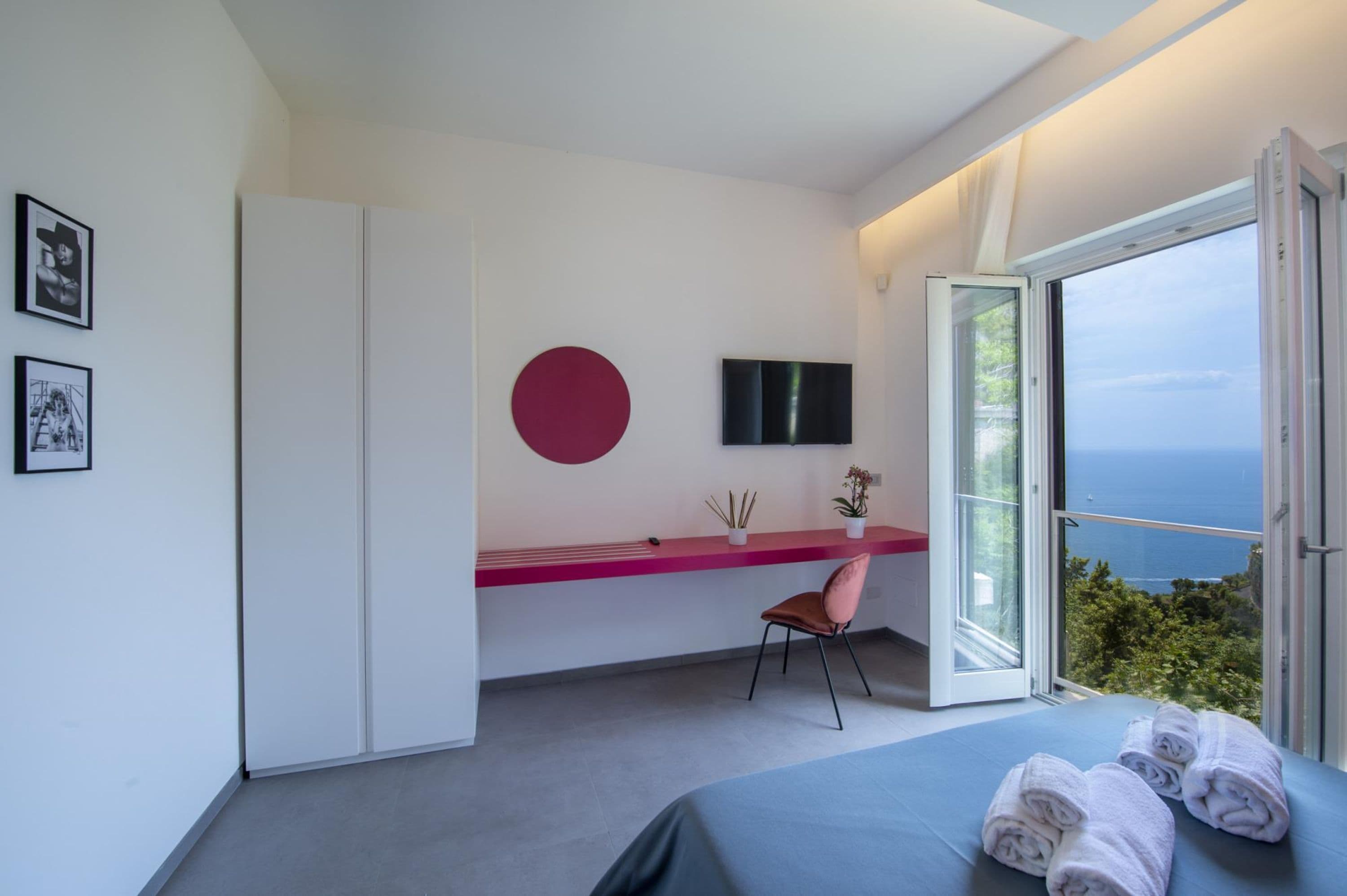 A modern bedroom with a bed, a desk, a chair, and a large window with a view.