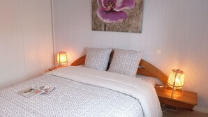 Un letto rifatto con biancheria a motivi, due cuscini e una rivista sopra. Sono presenti due lampade da comodino e un quadro di fiori appeso al muro.