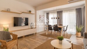 Uma sala de estar moderna com televisão de tela plana, mesa de jantar, cadeiras e sofá.