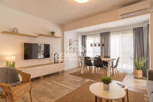 A modern living room with a flat-screen TV, dining table, chairs, and a sofa.