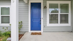 Ein Haus mit blauer Tür, weißen Fensterläden und einer Fußmatte.